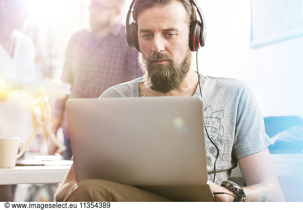 Serious männlichen Design-Profi mit Kopfhörer mit Laptop im Büro