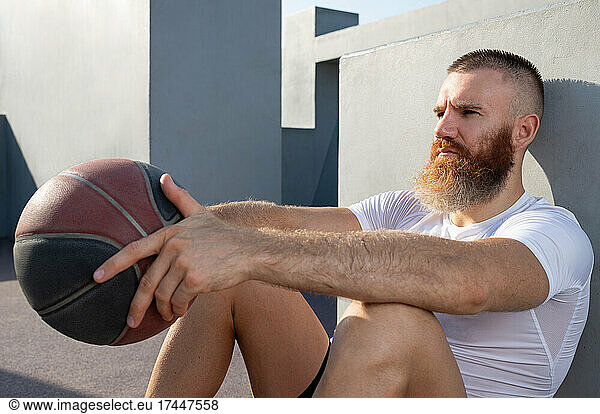 Serious male athlete with ball resting near wall