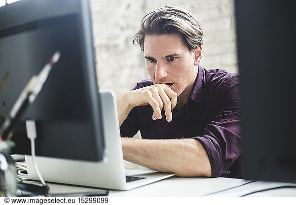 Serious male IT professional thinking while coding in laptop at creative workplace
