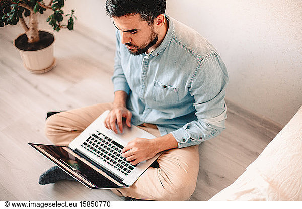 Serious man using laptop computer while sitting on floor at home
