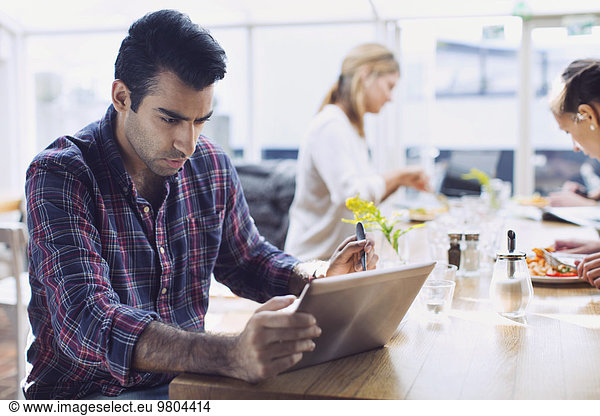 Serious Mann mit digitalen Tablet mit Freunden im Hintergrund im Cafe