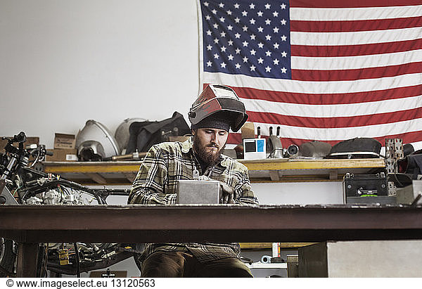 Serious manual worker working on machinery against American flag at auto repair shop
