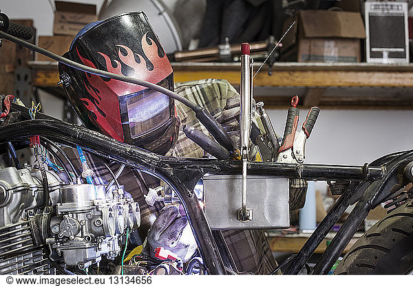 Serious mechanic welding metal of motorcycle engine at auto repair shop