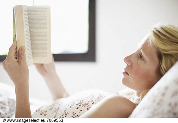Serious mid adult woman lying on bed and reading book