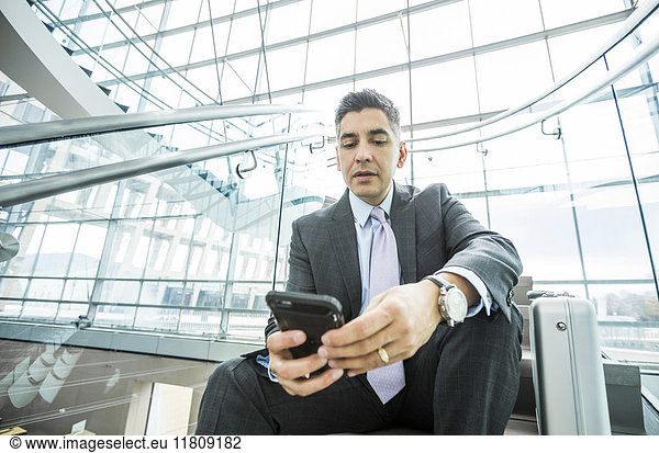Serious Mixed Race Geschäftsmann sitzt auf Treppe texting auf Handy