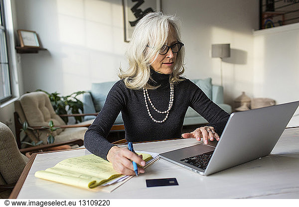 Serious senior woman using laptop computer while paying bills at home