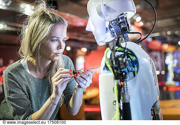 Serious tech developer working with screwdriver on human robot at workshop