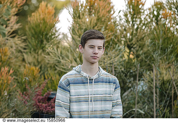 Serious teen boy in blue striped sweatshirt with plants in background