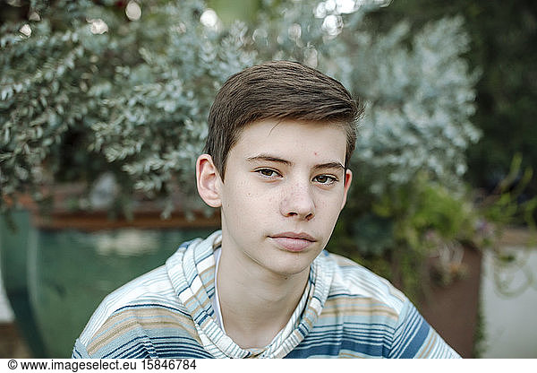 Serious teen boy wearing blue striped shirt with potted plant in back