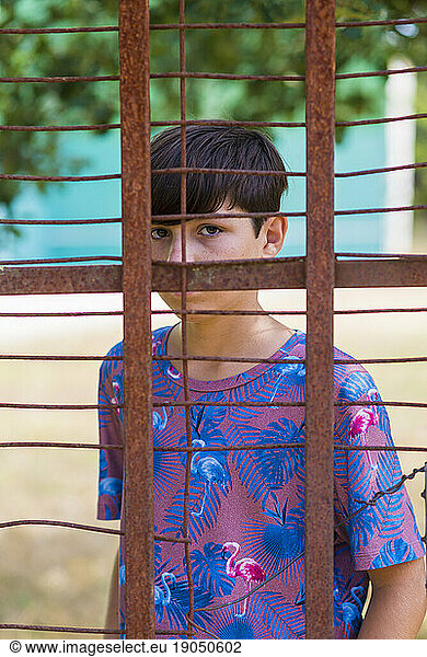 serious teen in casual wear behind metallic fence outdoors