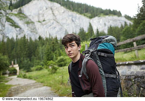 serious teenager with a backpack on a trail in the mountains