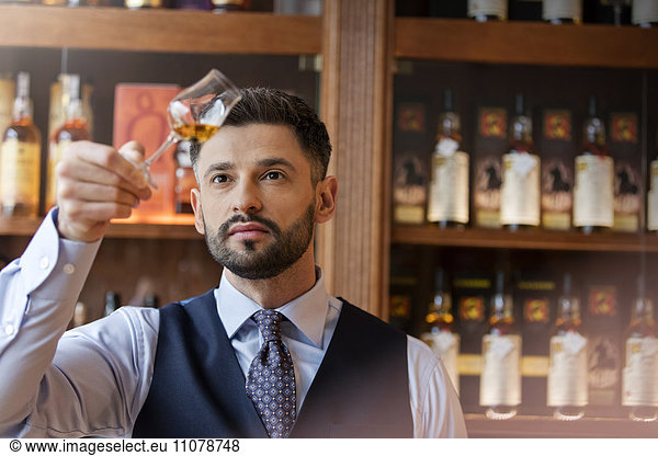 Serious well-dressed bartender examining whiskey