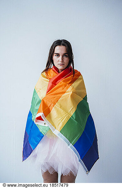 Serious woman covered in rainbow flag standing in front of wall