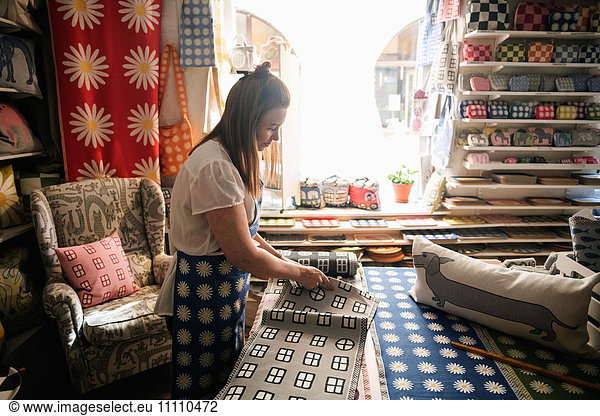 Serious woman cutting fabric swatch while working in shop