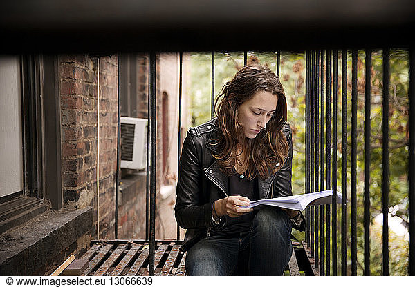 Serious woman reading book while sitting at fire escape