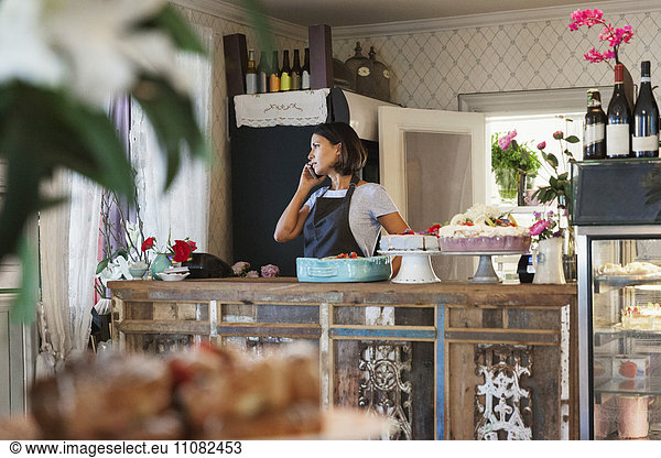 Serious woman talking on phone while standing by counter at cafe