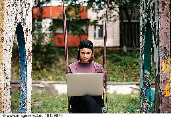 Serious young female student using laptop sitting on a swing