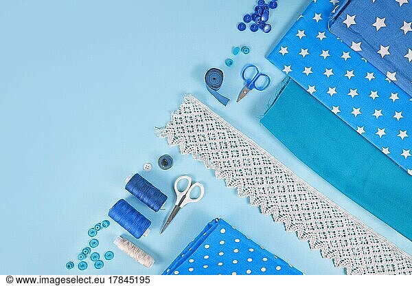 Sewing flat lay with various tools like fabric  scissors  spools and ribbons on blue background