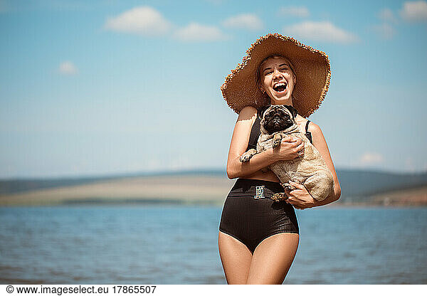 Sexy girl in a wide hat with a pug on the beach
