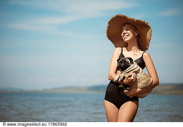 Sexy girl in a wide hat with a pug on the beach