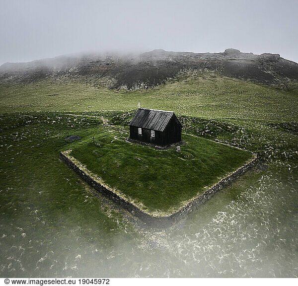 Shabby black church surrounded by hills on misty day