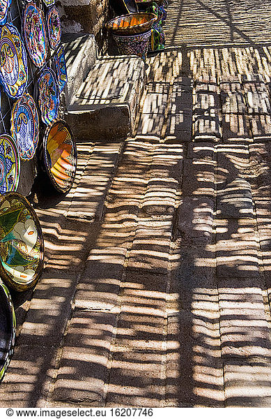 Shadows and shade patterns falling on a pavement  pottery bowls on display