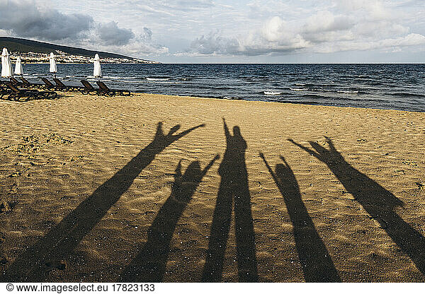 Shadows of five people standing on sandy beach with raised arms