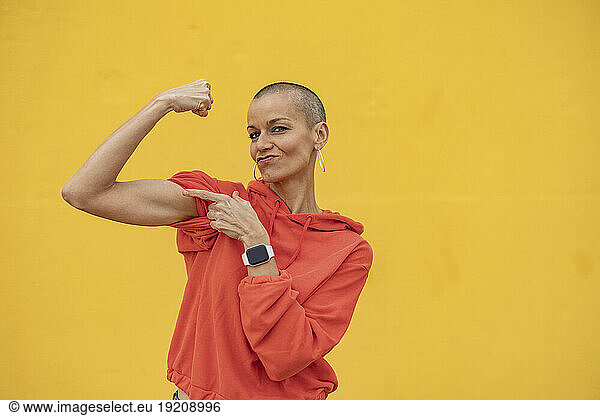 Shaved head woman flexing muscles in front of yellow wall