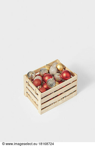 Shiny christmas baubles in wooden box against white background