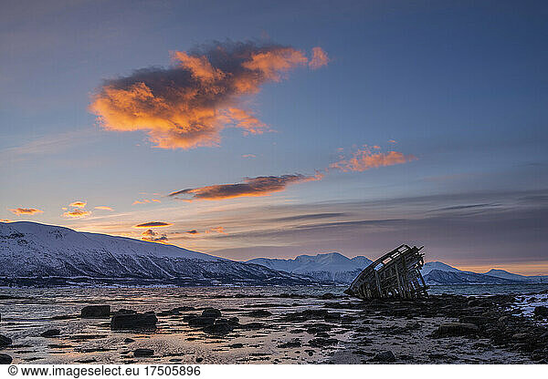 Shipwreck lying on shore of secluded Fjord at winter dawn