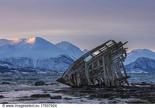 Shipwreck lying on shore of secluded Fjord at winter dawn