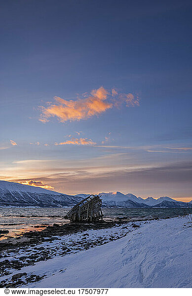 Shipwreck lying on shore of secluded Fjord at winter dawn
