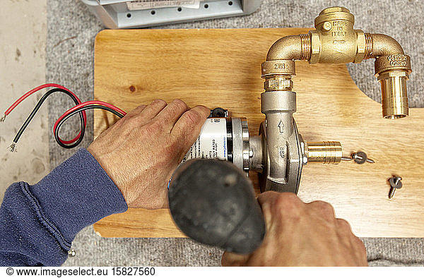 Shipwright installing a water pump system on a wooden board