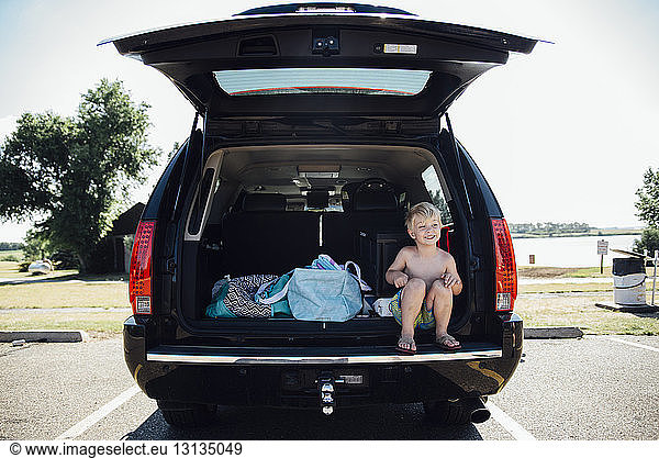 Shirtless boy looking away while sitting on car trunk