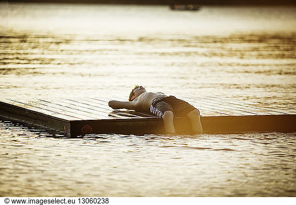 Shirtless boy lying on floating platform in lake during sunset