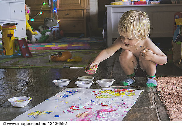 Shirtless boy with watercolor paints making apple prints on white paper at home