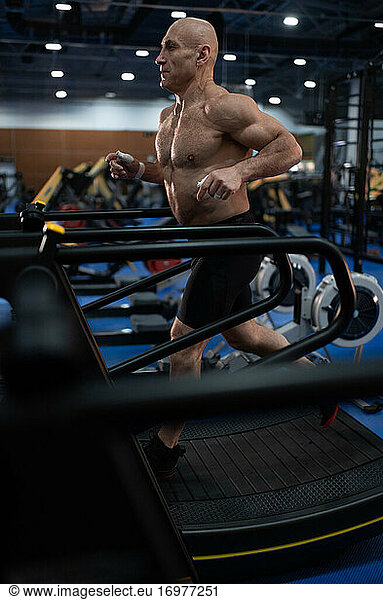 Shirtless elderly athlete exercising on treadmill
