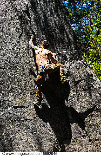 Shirtless fit climber getting to the top of the boulder