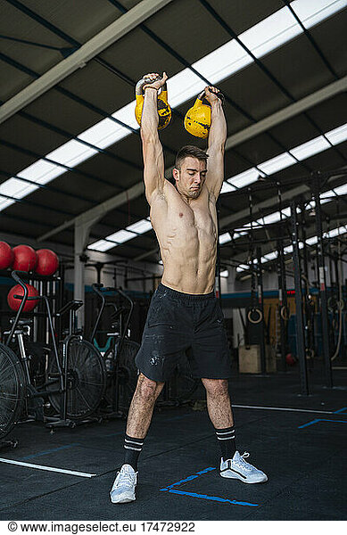 Shirtless male athlete holding kettlebells while working out