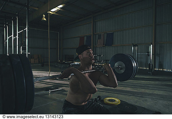 Shirtless male athlete lifting barbell in gym