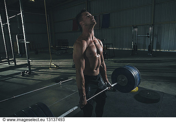 Shirtless male athlete lifting barbell in health club