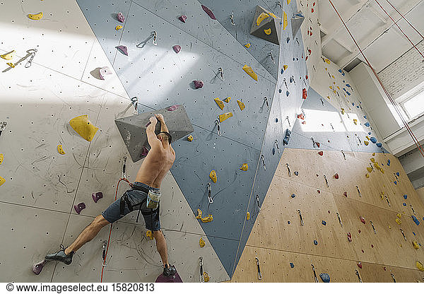 Shirtless man climbing on the wall in climbing gym