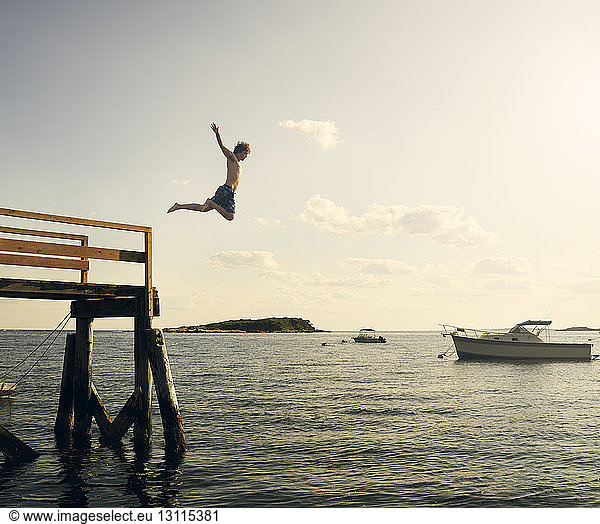 Shirtless man diving into sea from pier against sky