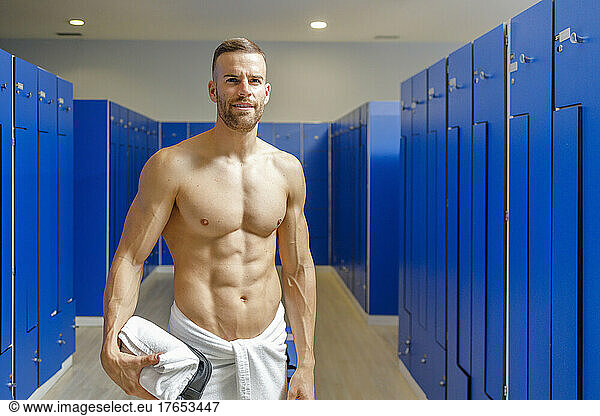 Shirtless man holding towel standing in changing room