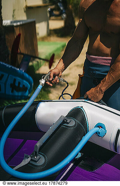 Shirtless man inflating hydrofoil at beach