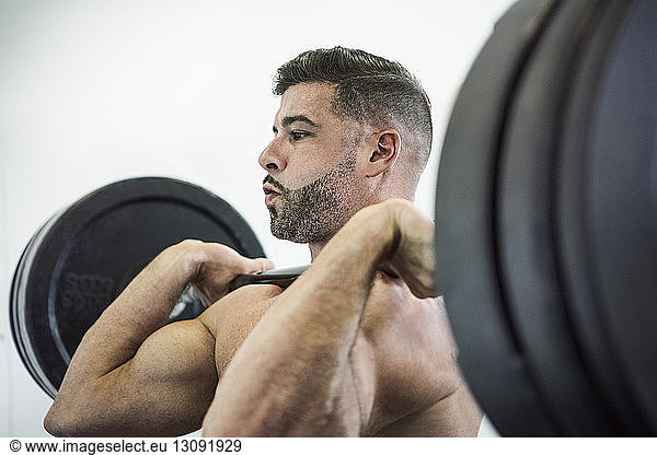 Shirtless man lifting barbell in crossfit gym