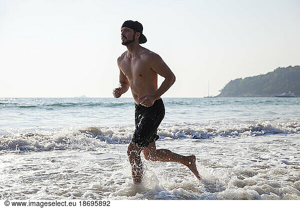 Shirtless man running in water at beach