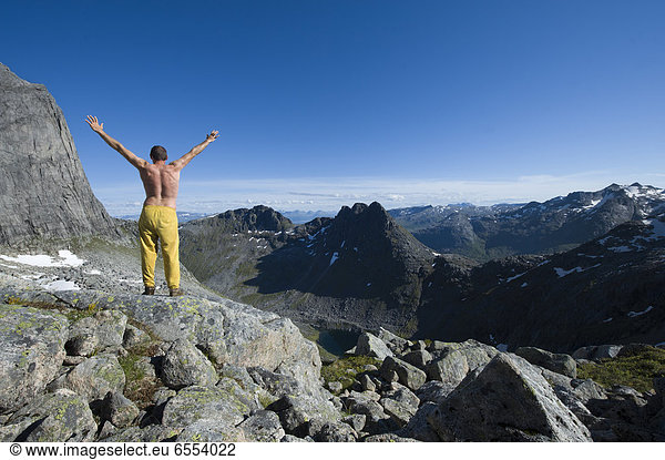 Shirtless man standing on mountain peak with arms raised