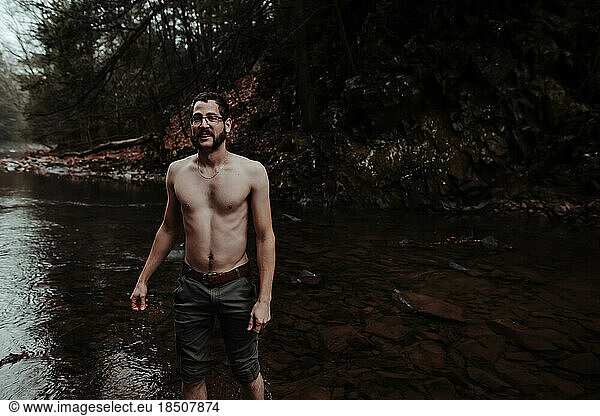 shirtless man wading in a cold creek in November