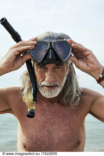 Shirtless mature man holding snorkeling glasses at beach